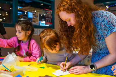 Kirsty writing something on a piece of paper and a child looking over intently.