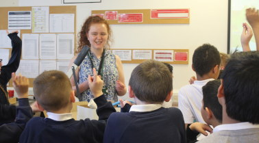 Kirsty presenting to an audience of children with their hands up.