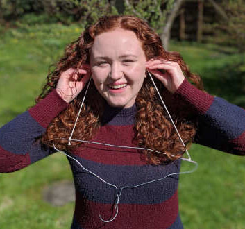 Kirsty holds string to her ears, from which hangs a metal coat hanger.