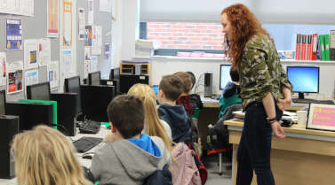 Kirsty looking over several children sat at desktop computers.