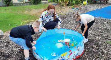 Kirsty and a young girl and boy shake the sides of a paddling pool to test their craft boats.