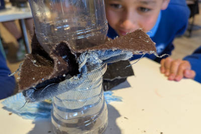 A child is filtering dirty water through layers of sample material in between parts of a plastic cup. They are looking intently to see if the materials can trap the dirt. 